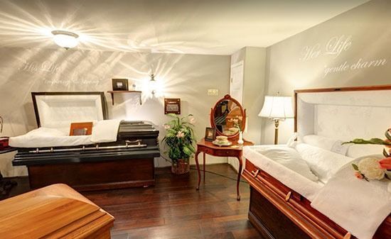 A display room featuring multiple wooden caskets, an ornate dressing table with a mirror, and a table lamp.
