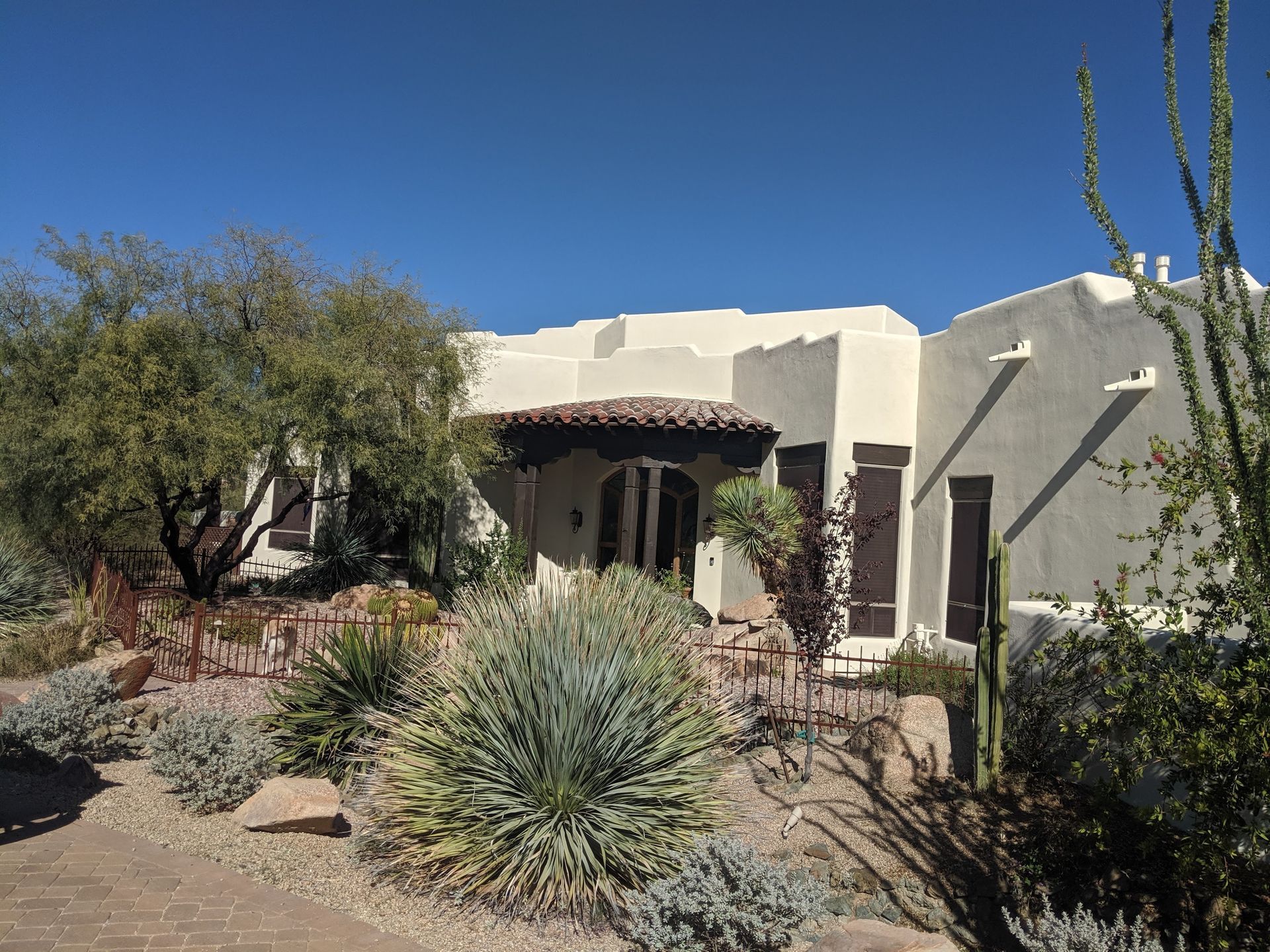 Southwestern-style house with stucco exterior, dark shutters, and drought-tolerant landscaping under a clear blue sky.