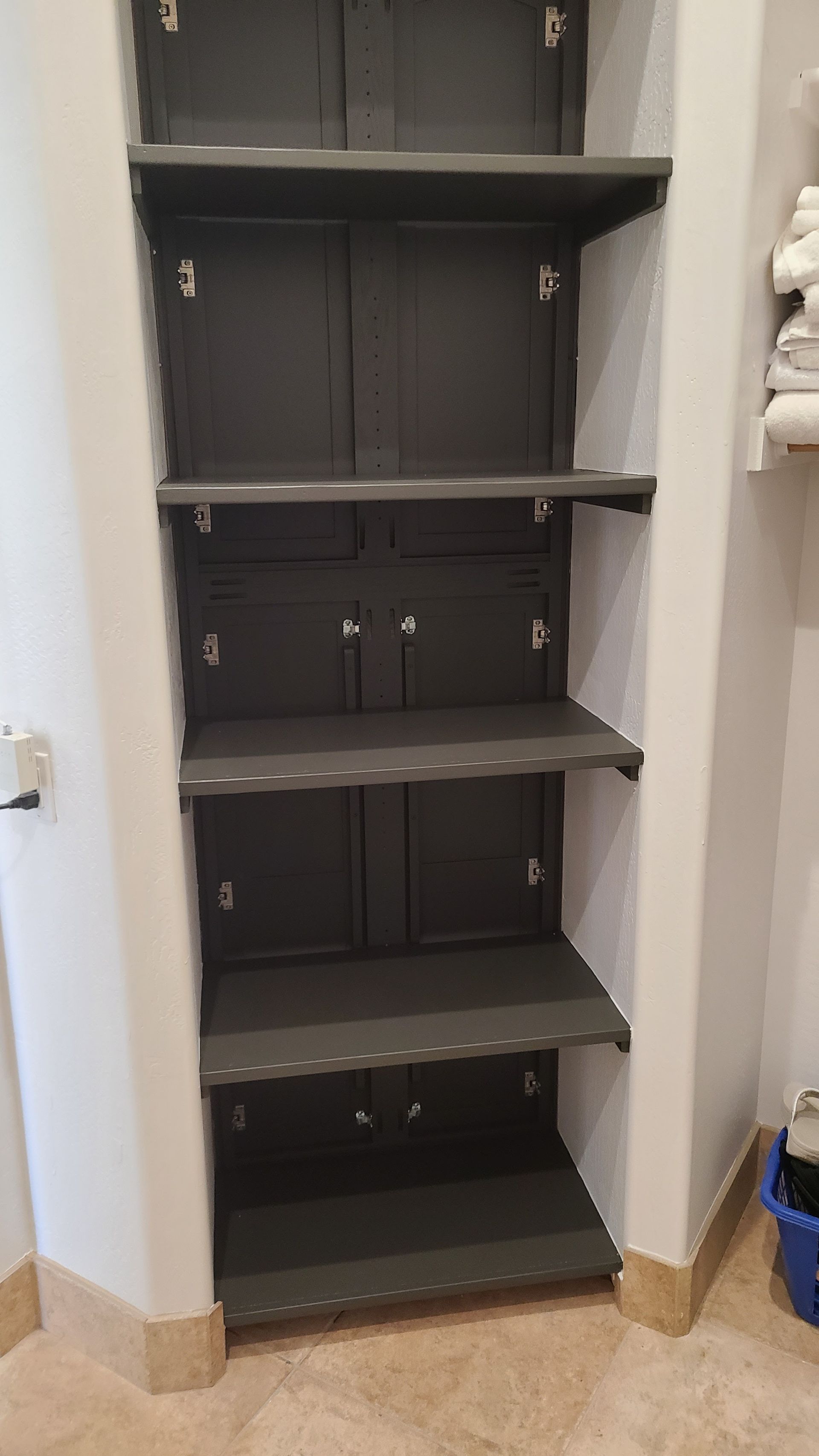 Gray built-in shelving unit with closed cabinet doors and open shelves, recessed in a white wall.