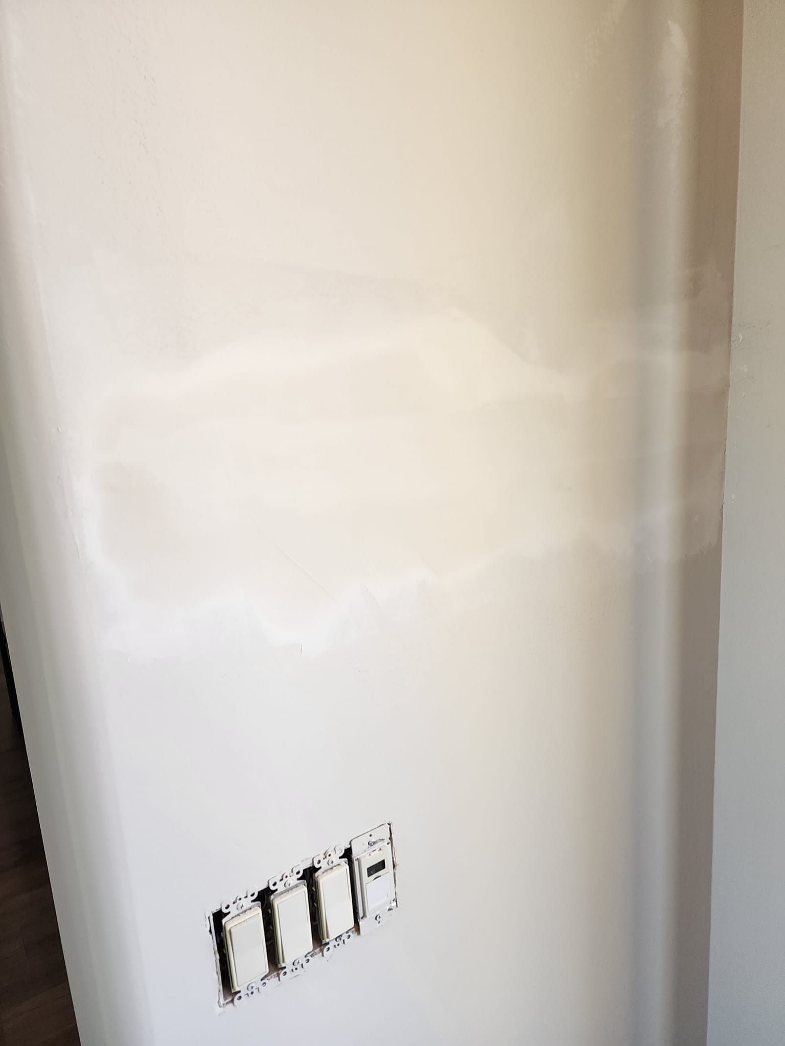 White wall with a patched area, electrical outlet, and a corner.