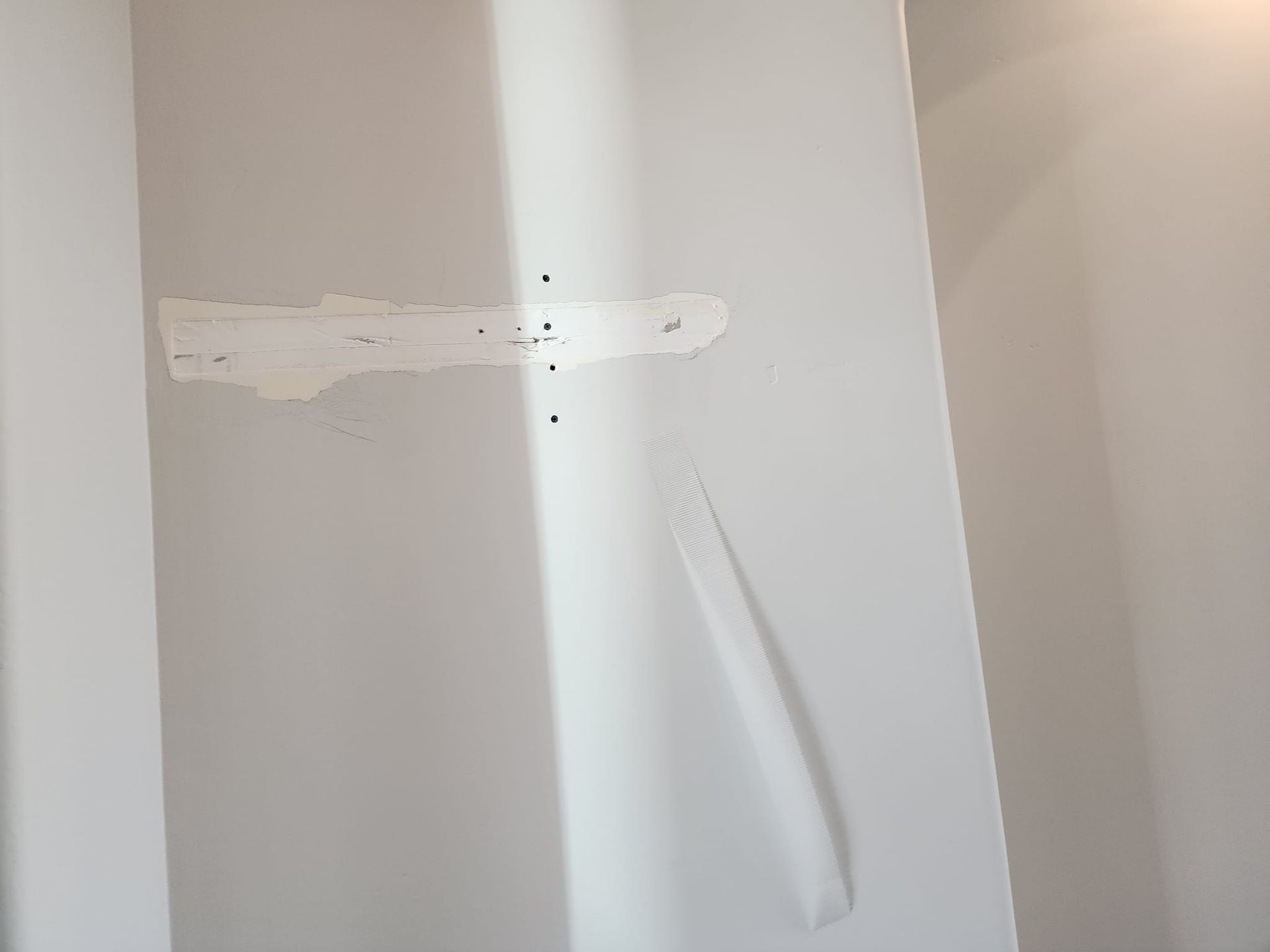 Drywall repair: Patch with visible screws, pale gray wall, and white compound.