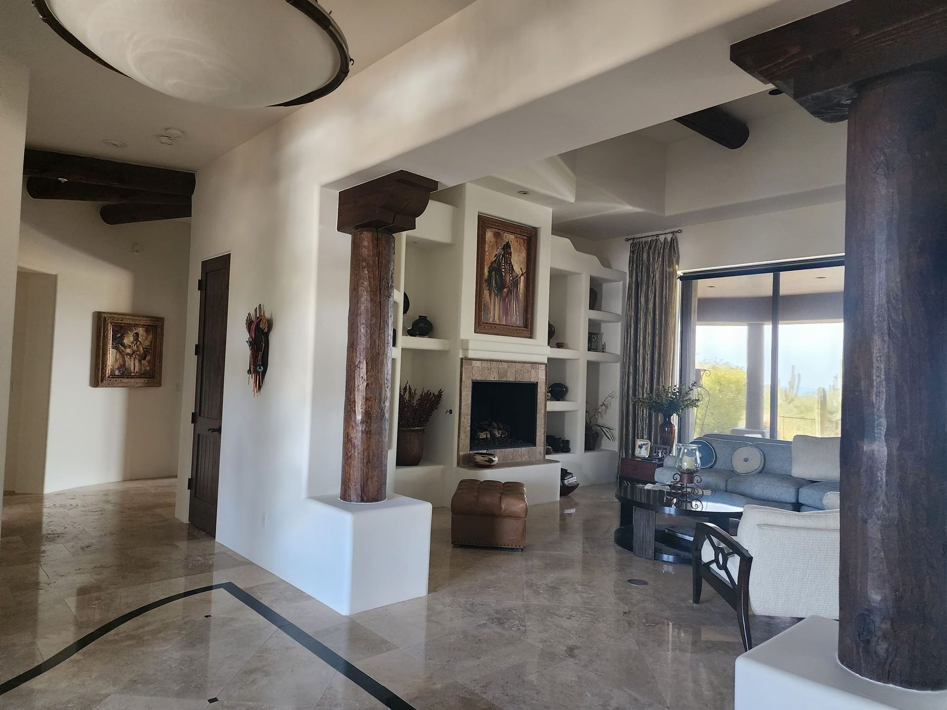 Spacious interior with exposed wooden beams, fireplace, columns, artwork, and large windows with a view.