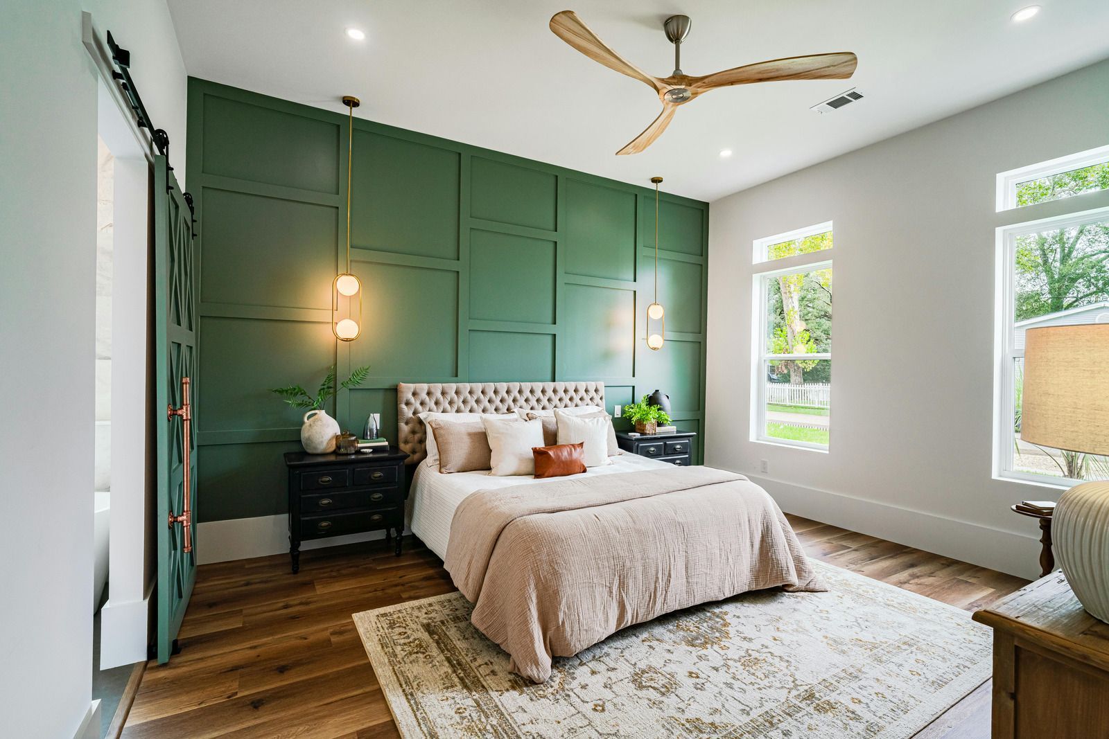 Bedroom with green paneled wall, beige bed, sliding barn door, and a wooden ceiling fan.