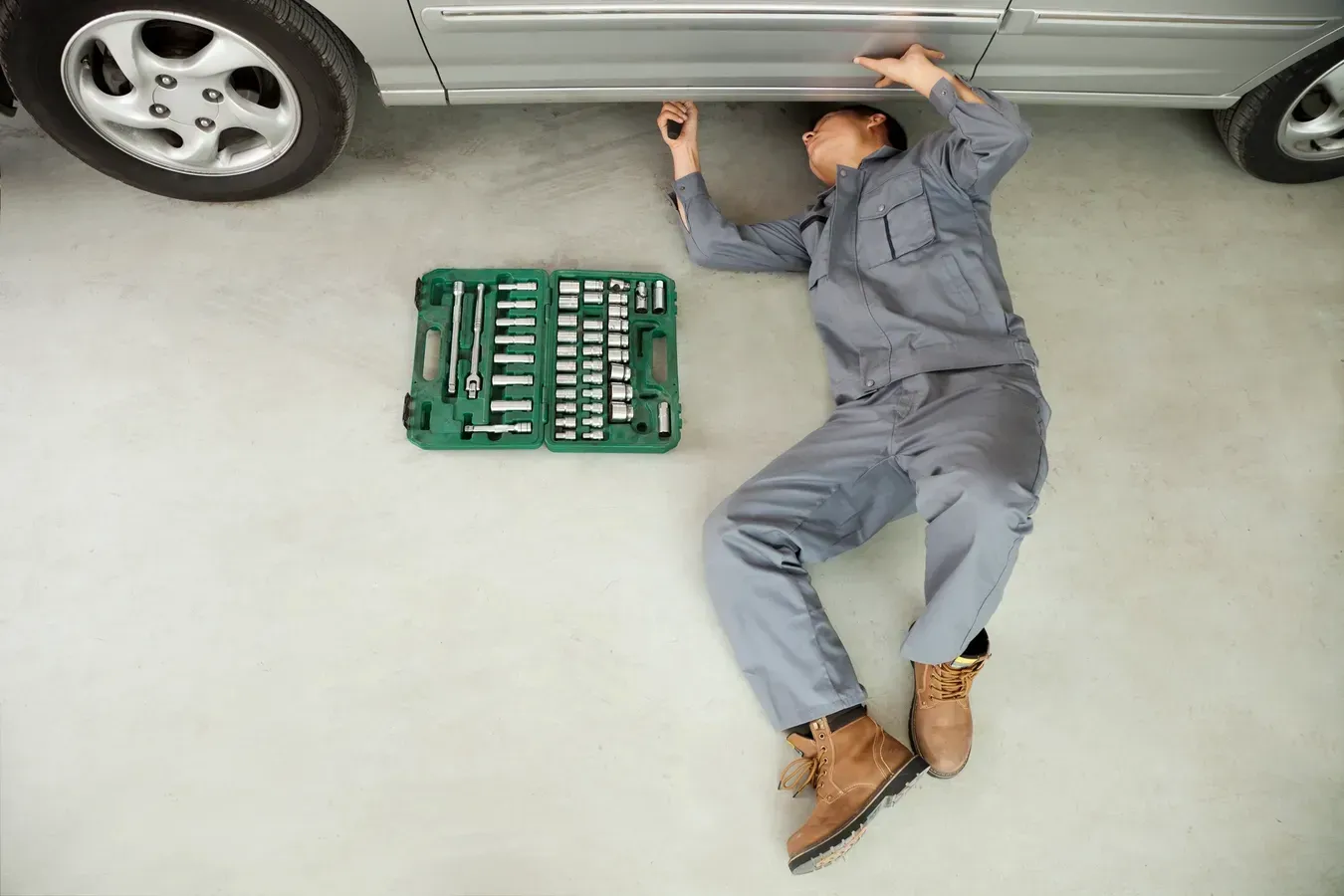 A man is laying on the floor under a car in a garage.  | Royal Expert Auto Service & Discount Tire Center