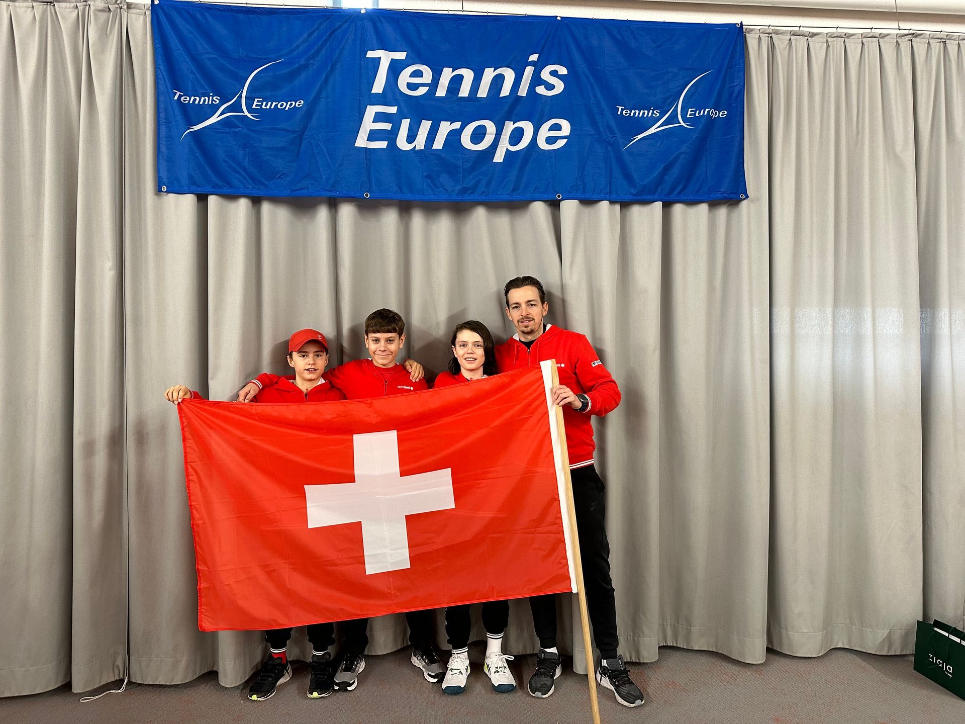 Eine Gruppe von Menschen hält eine Schweizer Flagge vor einem Tennis-Europe-Banner
