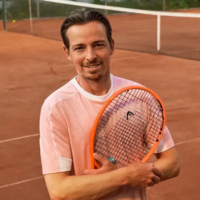 Ein Mann in einem blauen Hemd hält einen Tennisschläger