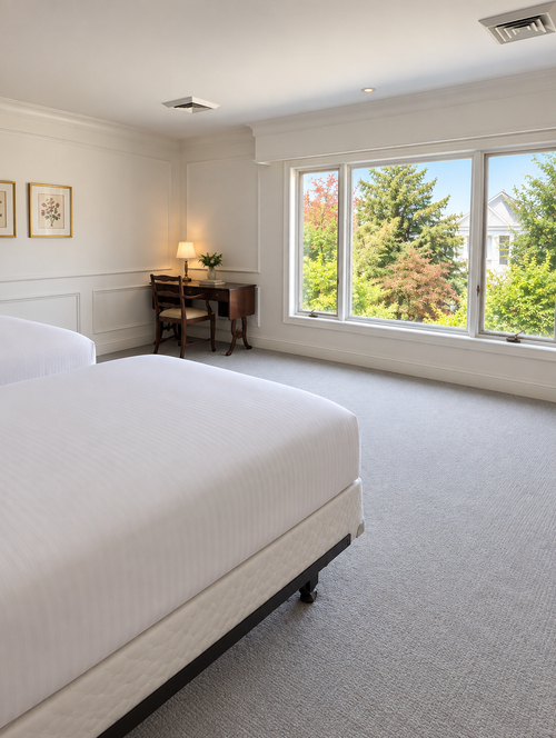 Bright bedroom with a white bed, desk lamp, and large windows overlooking greenery.