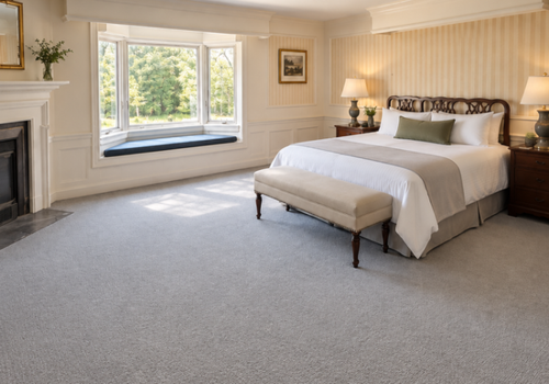 Bright bedroom with a large bed, bench, fireplace, and window seat overlooking greenery