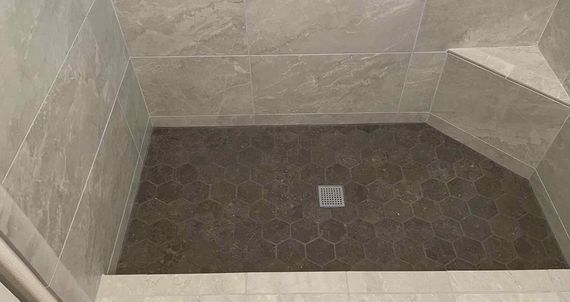 Tiled shower stall with a small square drain in the center and beige-gray walls.