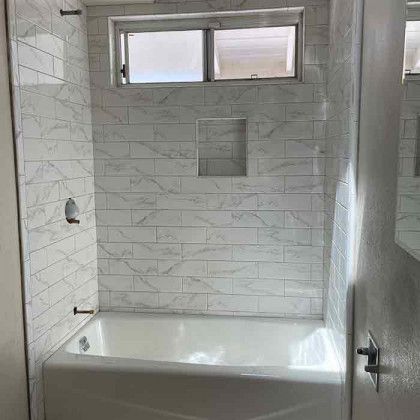 Small white-tiled bathroom with a bathtub, shower fixtures, and a frosted window above the tub