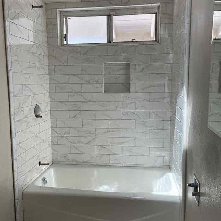 White tiled bathtub and shower alcove with frosted window and built-in niche.