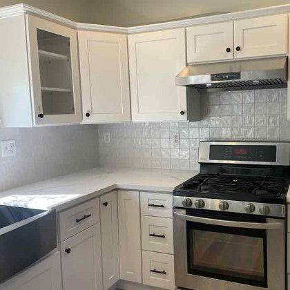 White corner kitchen with cabinets, tiled backsplash, gray countertops, sink, and stainless gas range
