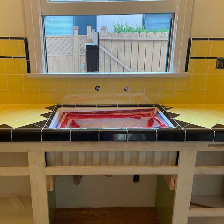 Partially tiled kitchen sink area with a red-lined opening beneath a window and backyard view