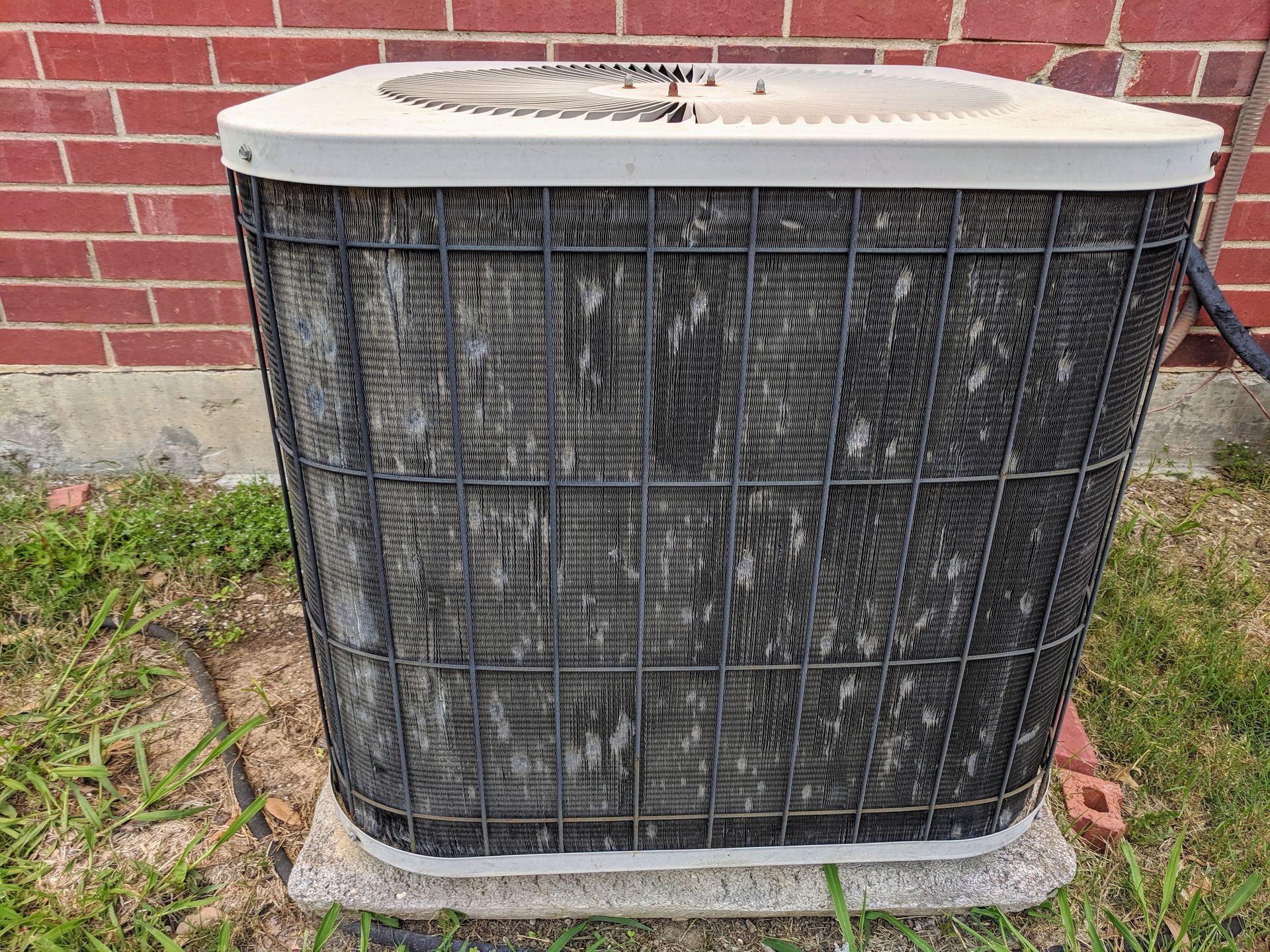 Dirty outdoor air conditioner unit against a brick wall.