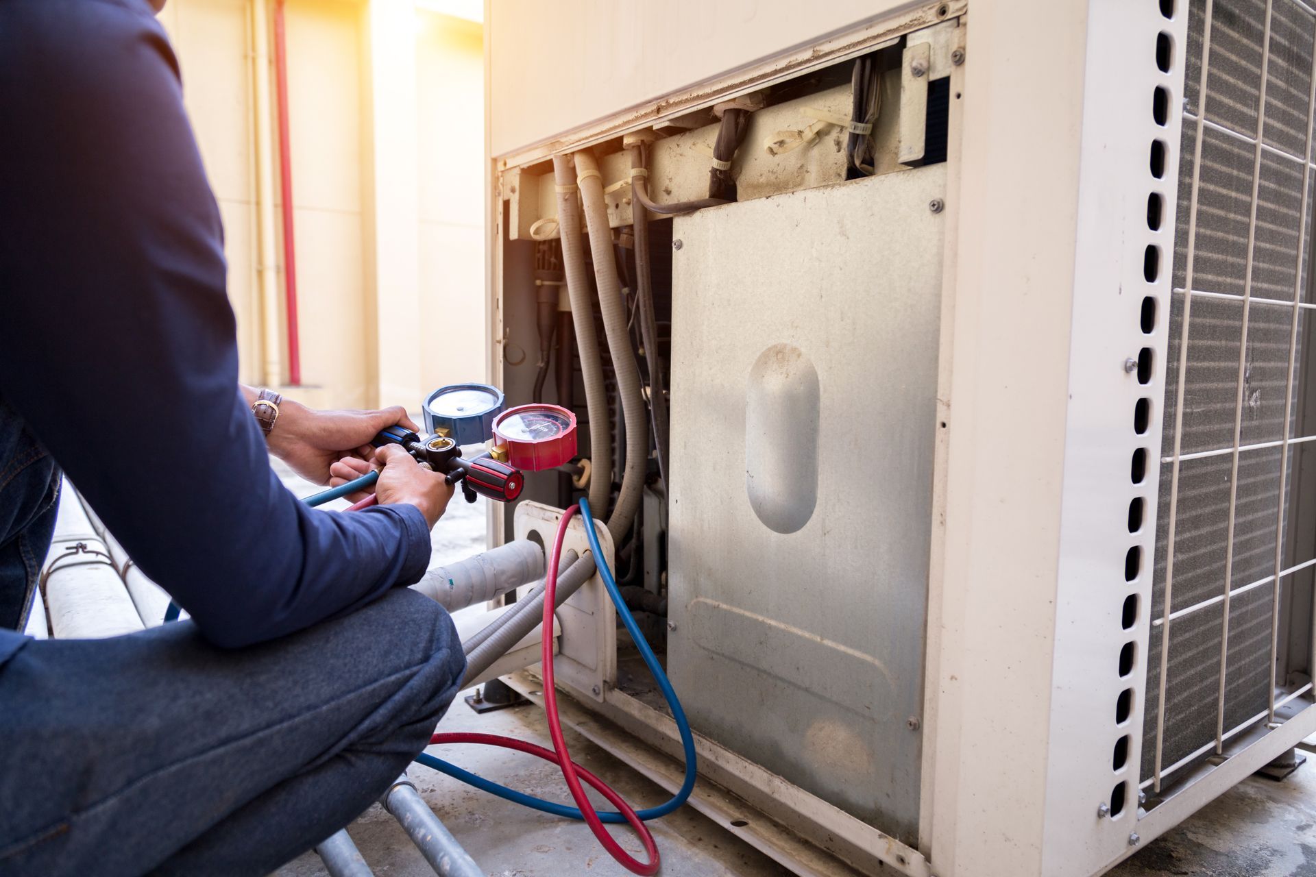 HVAC technician servicing an outdoor air conditioning unit with gauges and hoses.