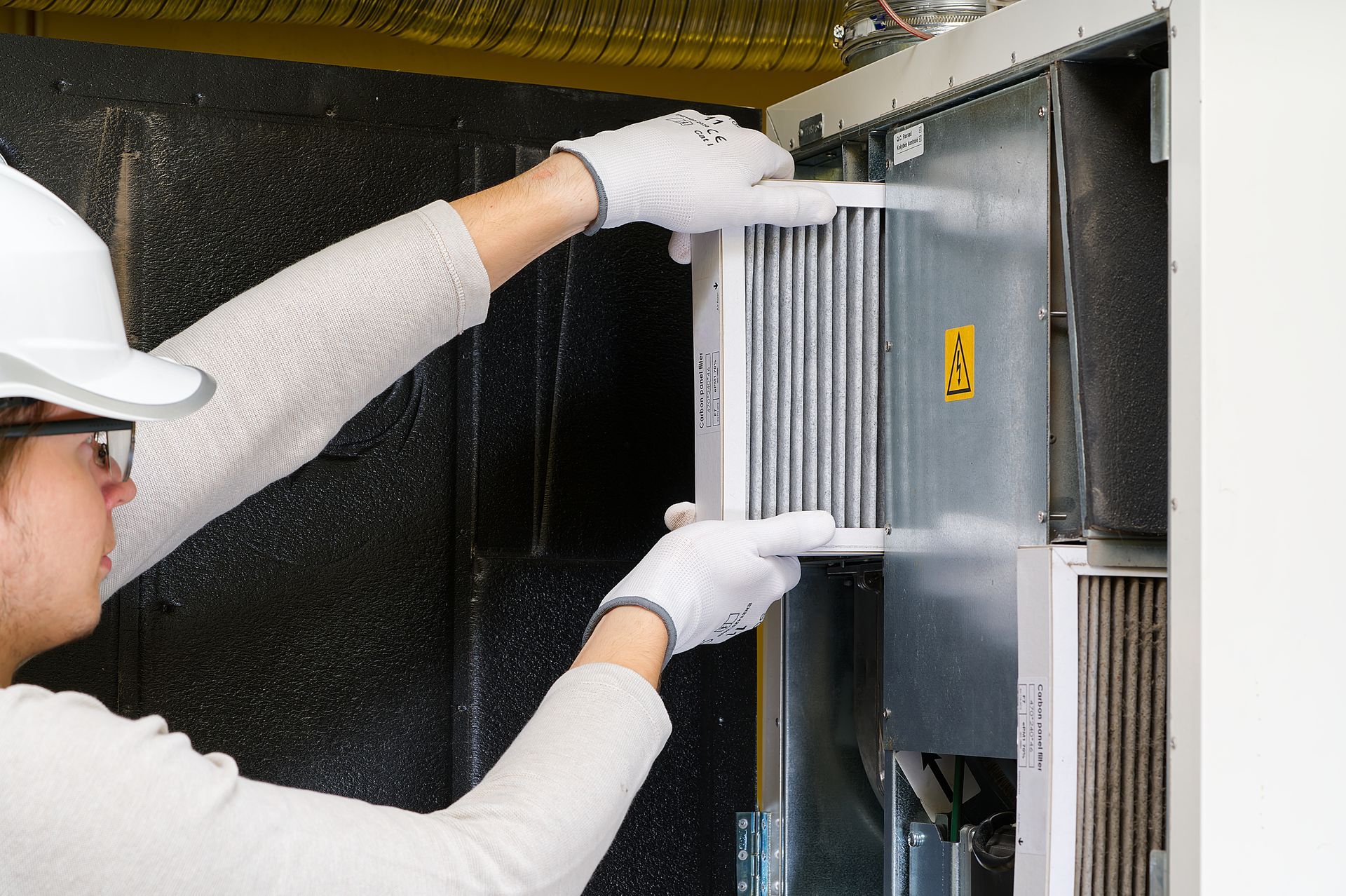 Person in gloves and hard hat installing air filter in a machine.