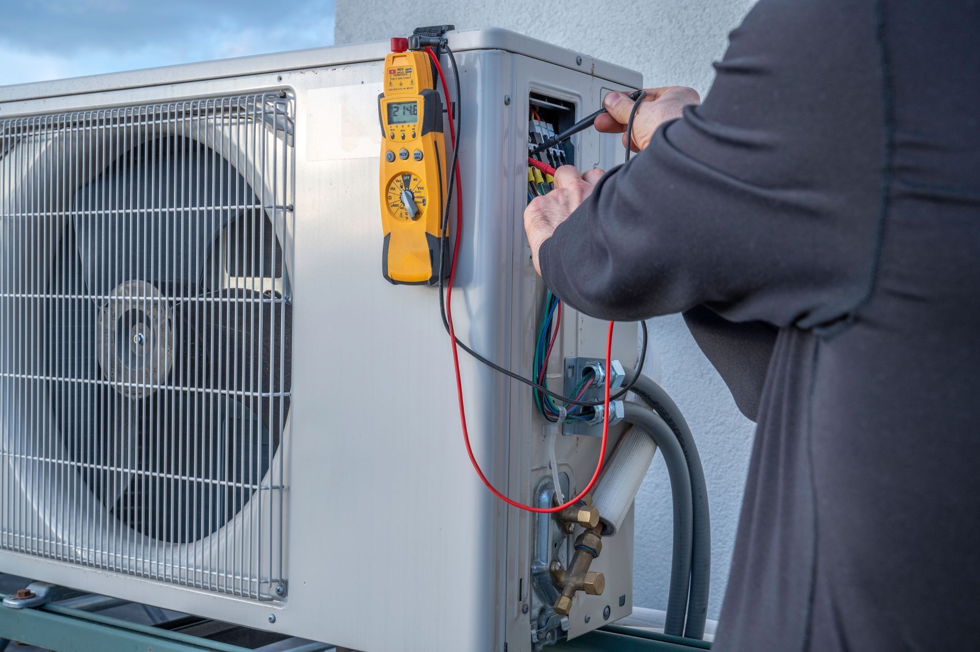 Person testing an air conditioning unit with a multimeter.