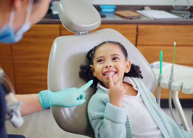 Dentist gently examining a smiling child in a dental chair, with gloved hands and dental tools visible
