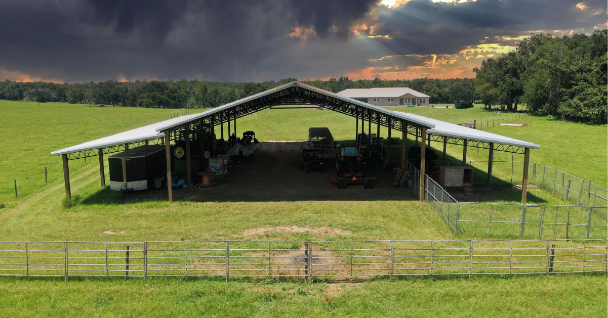 Open-sided barn in a grassy field under a cloudy sunset sky