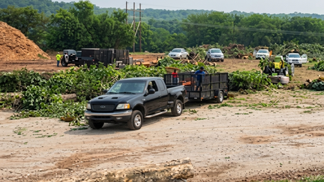 Pickup truck with trailer on a dirt lot, with several vehicles and people in the background.