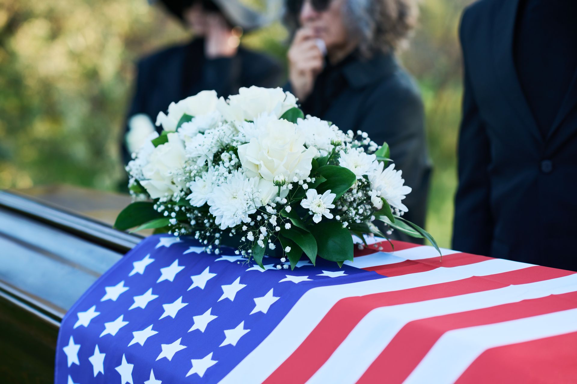 Woman holding a folded American flag and rose at a funeral, surrounded by mourners.