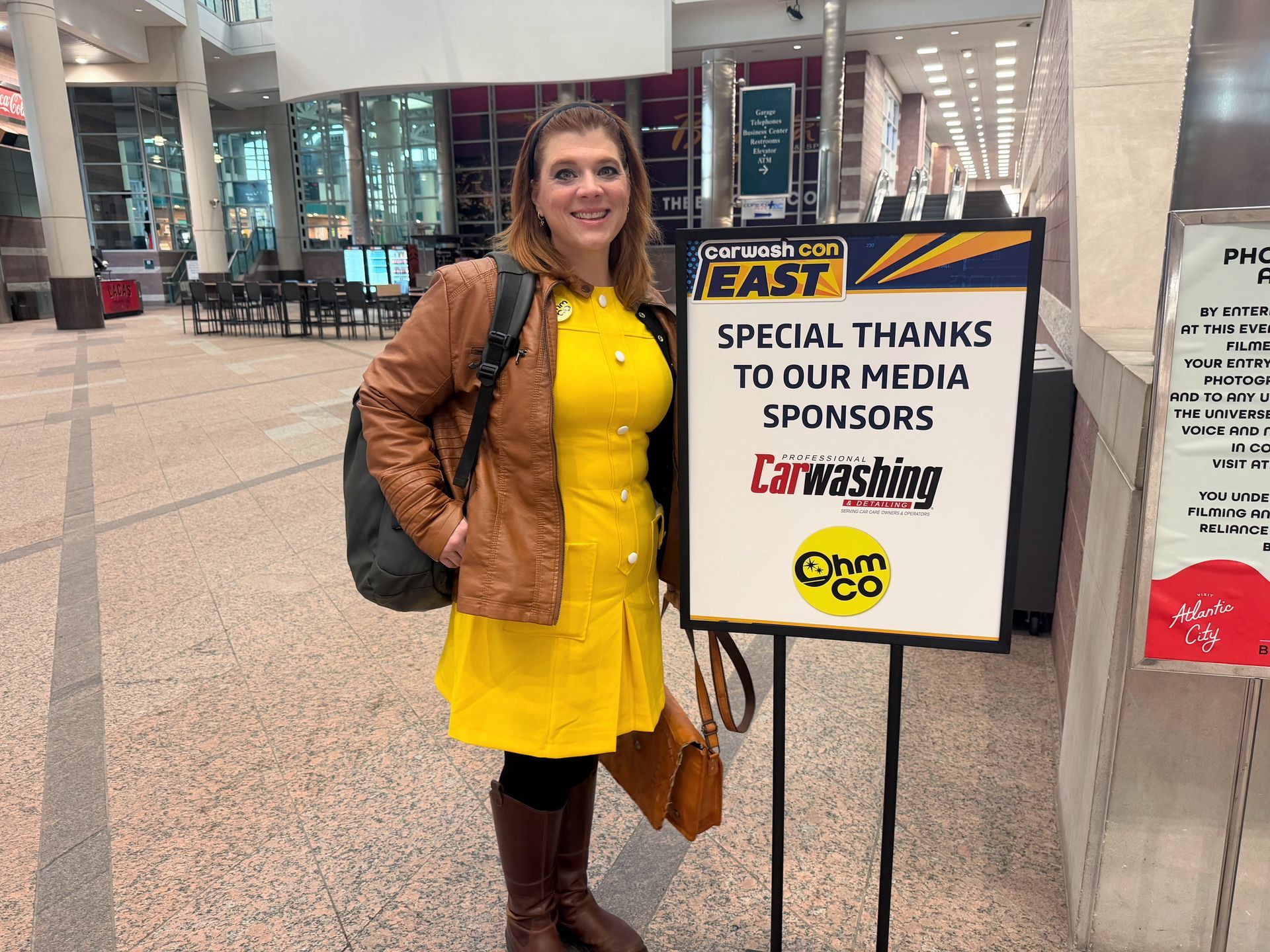 Mel Ohlinger standing beside the CarwashCon East media sponsors sign featuring OhmCo