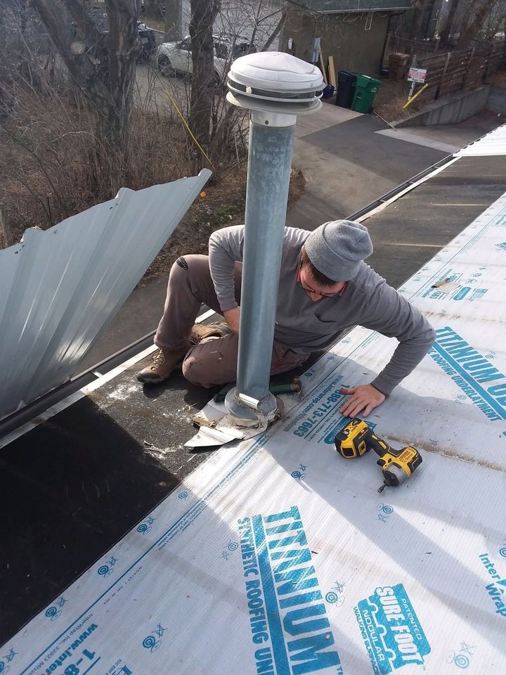 Worker installing roof vent on a shingled roof with tools nearby