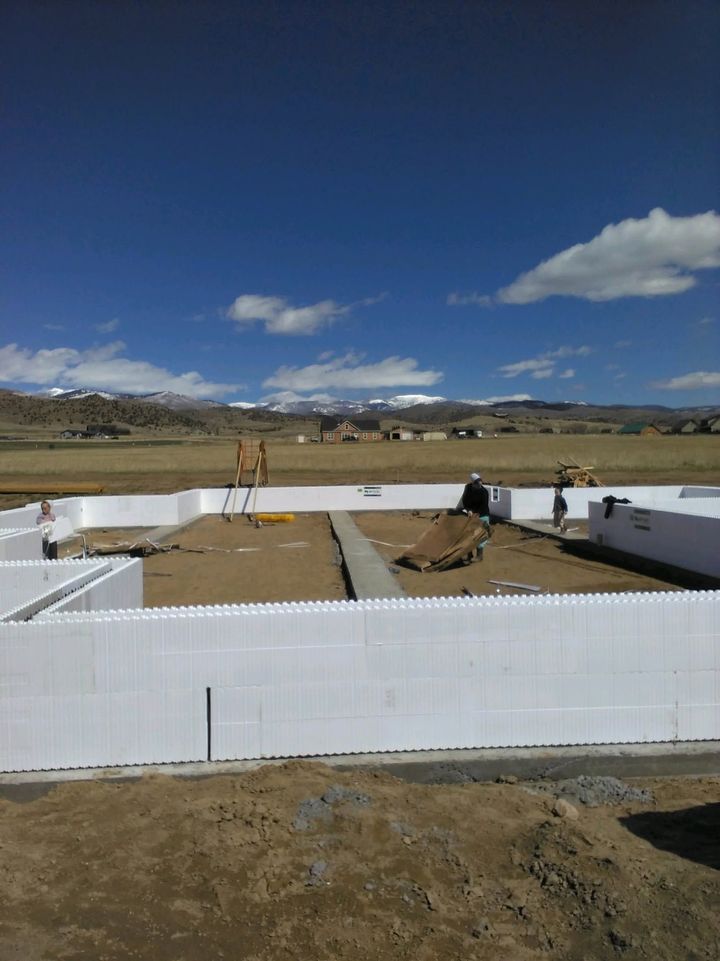 White foundation walls under construction in a rural field, with mountains and a blue sky in the background