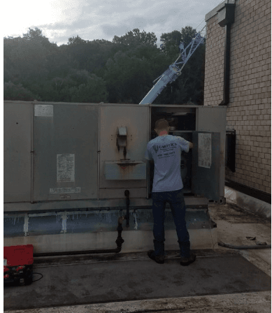 A man in a blue shirt is working on a machine outside of a building