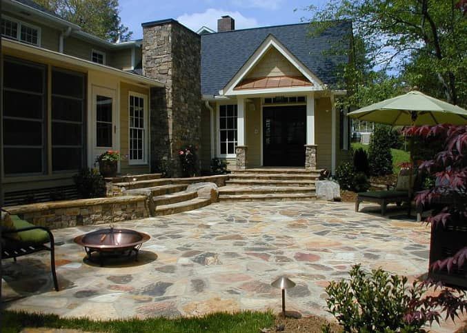 A patio with a fire pit and umbrellas in front of a house.