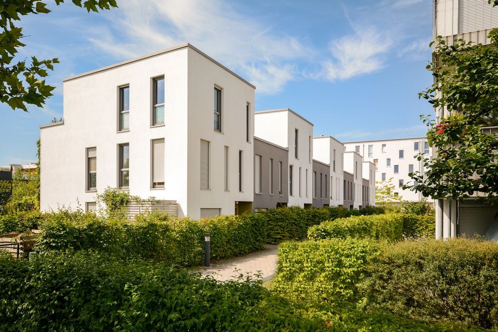 A row of white buildings with trees and bushes in front of them