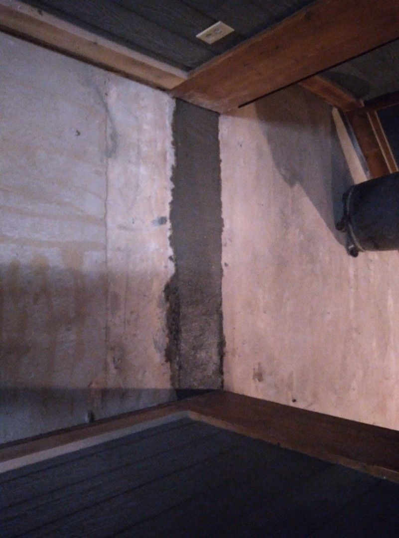 A corner of a room with a concrete wall and a wooden floor
