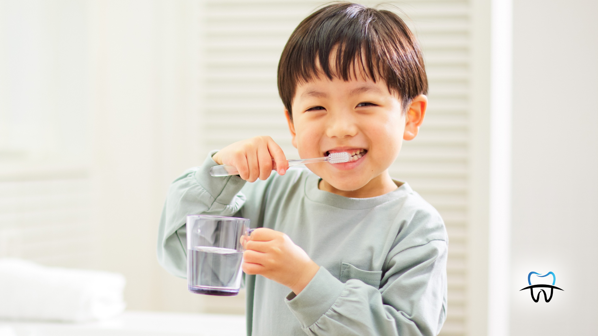 Young child brushing teeth with toothbrush and glass of water in bathroom.