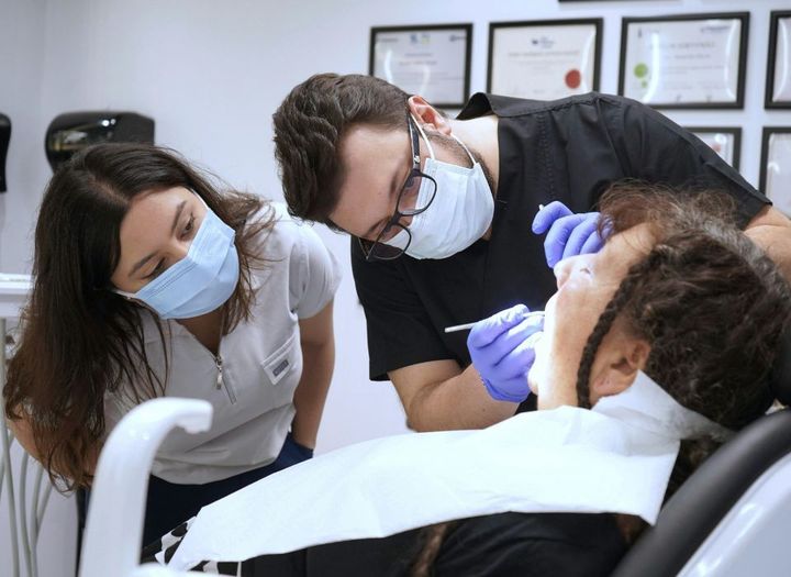 Dentist examining a patient with a hand on her cheek, expressing discomfort, in a dental office.