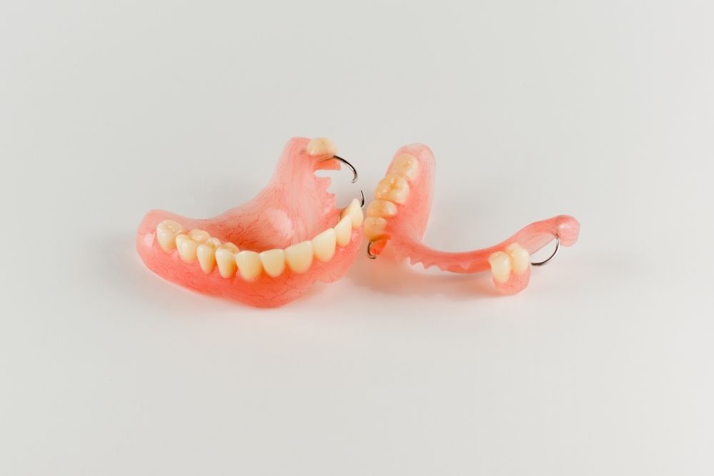 Partial dentures, pink and beige, on a white surface.