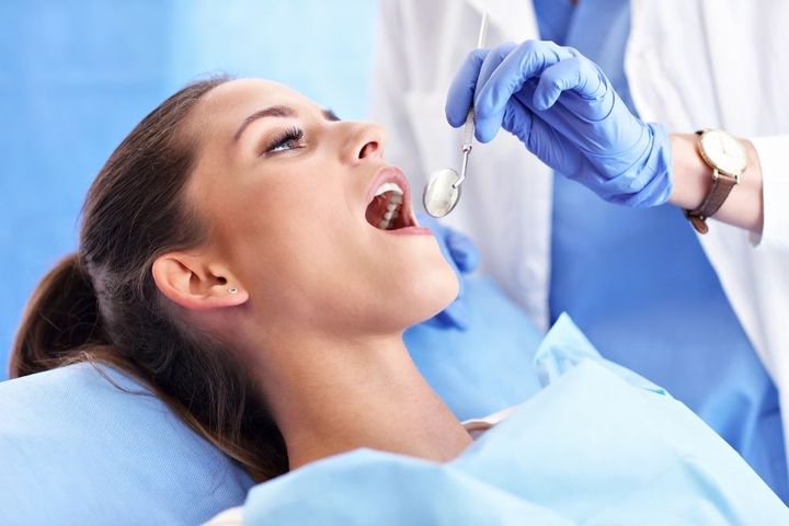 Dentist in green scrubs pointing at a screen with dental images, explaining to a patient in a dental chair.