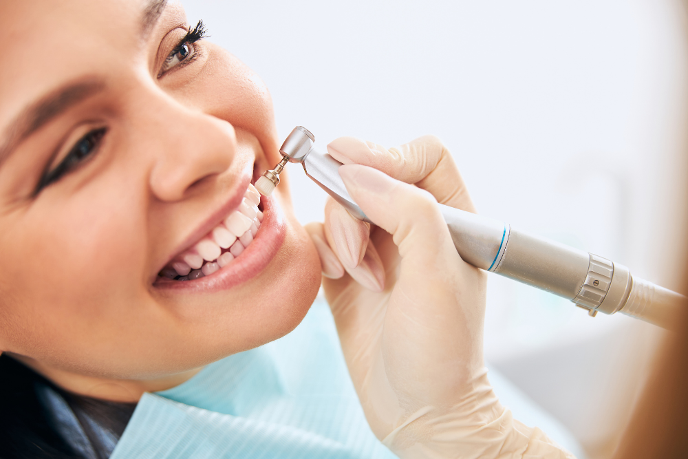 Woman getting dental cleaning, smiling, dentist's gloved hand holds a dental tool in her mouth.