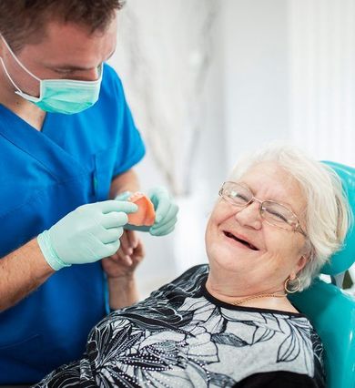 Dentist showing dentures to a smiling patient in a dental chair.