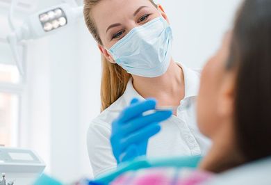 Dentist in mask and gloves examining patient's teeth with dental tools in bright office.