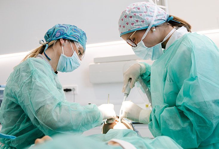 Two medical professionals in scrubs perform a procedure on a patient in a sterile environment.