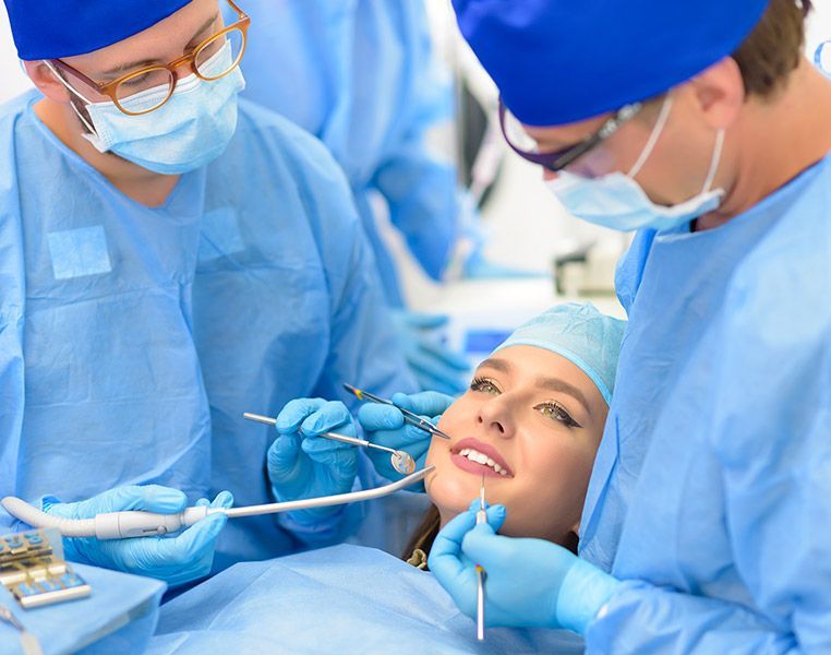 Dentists examining a patient's teeth during a procedure. Patient smiles while lying down.
