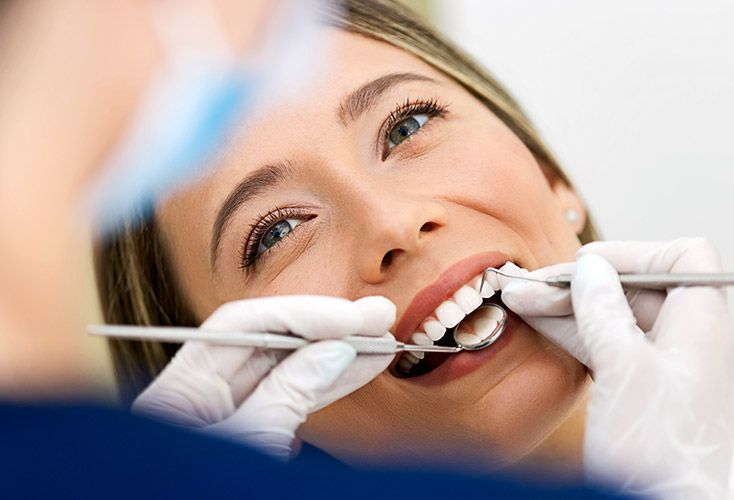 Woman smiling, having teeth examined by a dentist with tools and gloves.