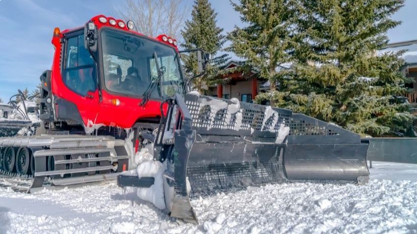 Person viewing the new MTN Equipment website on a laptop with a snow groomer in the background.
