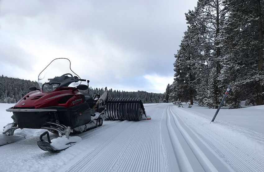 A snowmobile with a grooming attachment working on a ski trail, leaving freshly groomed snow behind.