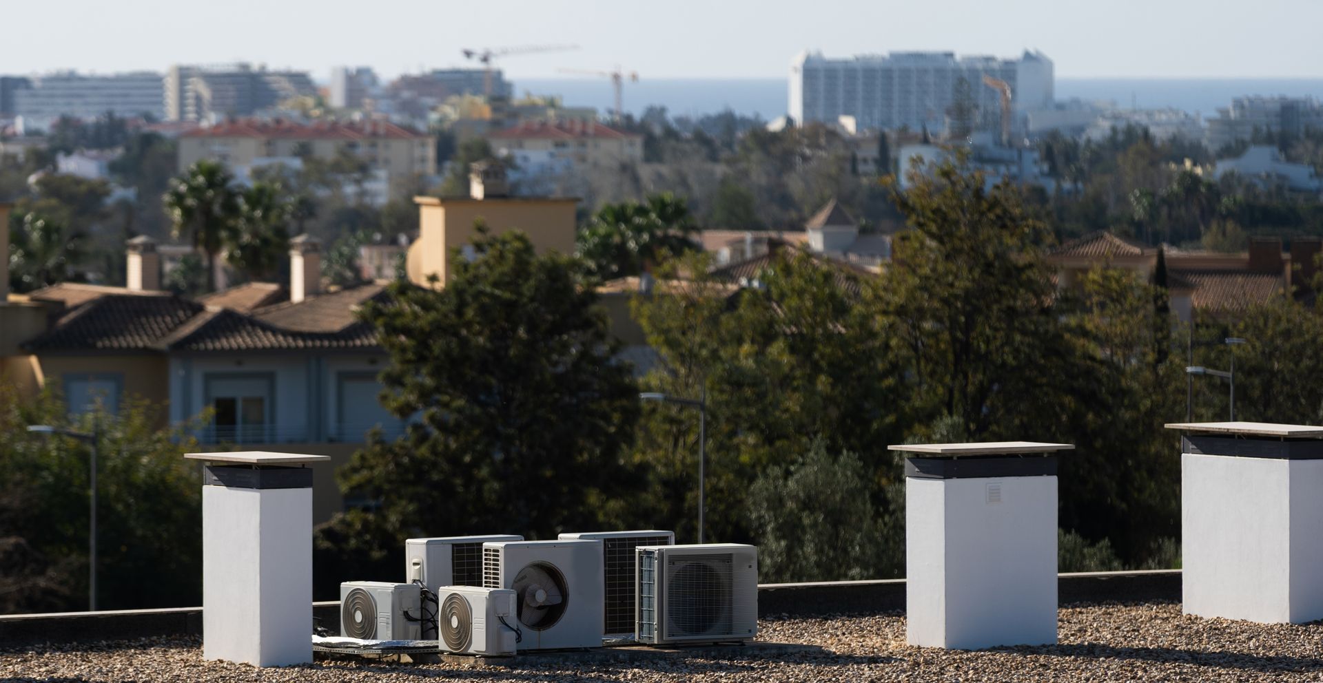 Rooftop HVAC units overlooking trees and low-rise buildings in a hazy cityscape