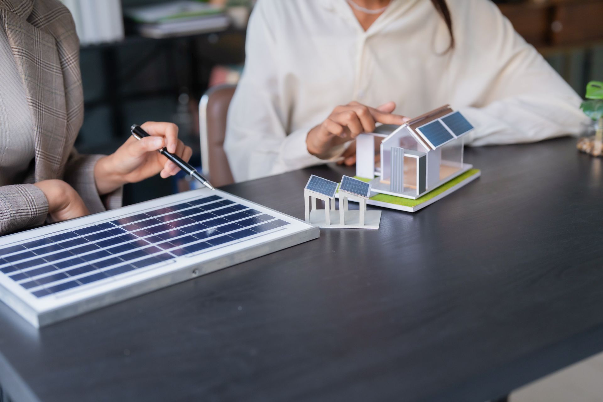 Two people examining a solar panel model and miniature house on a table