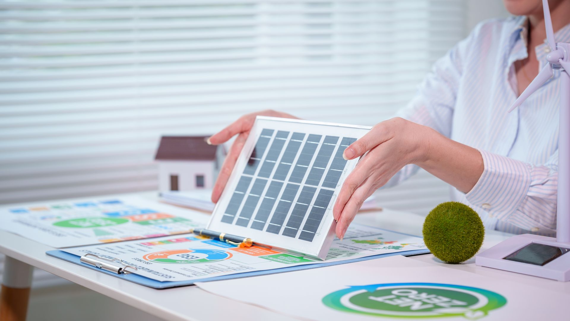 Person holding a solar panel model over charts and eco documents on a desk