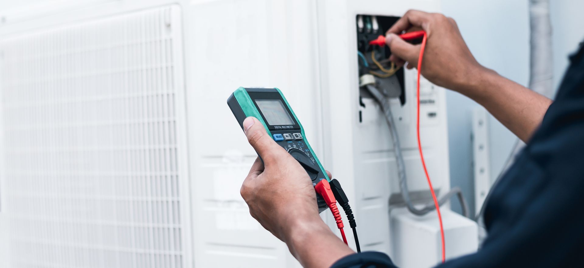 Technician testing electrical wiring with a multimeter beside a white panel