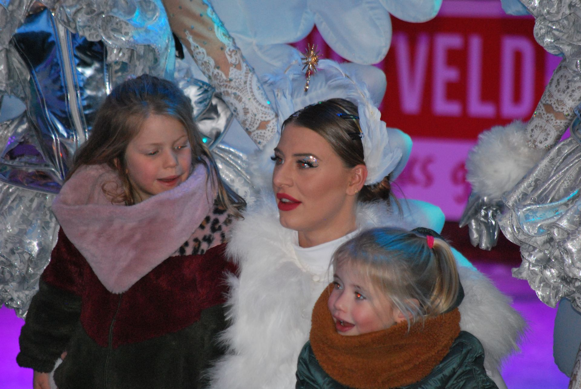Vrouw in witte bontjas met twee jonge kinderen. Toneelachtergrond met zilveren kostuums en 