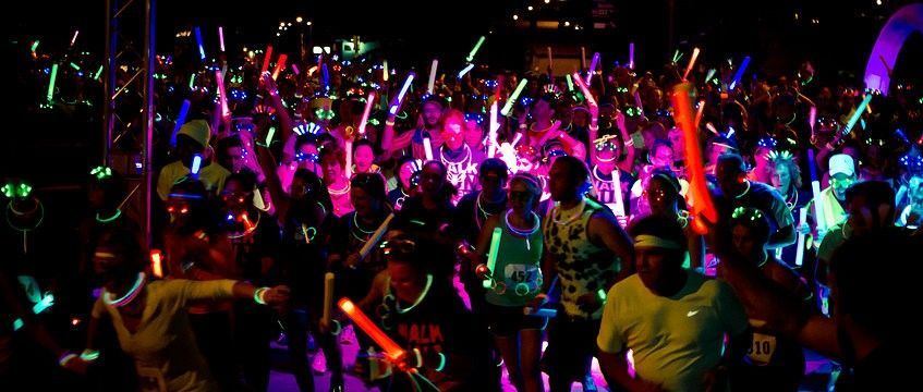 Een grote groep mensen met lichtgevende stokken in de nacht. Kleurrijke lichtjes verlichten de hardlopers.